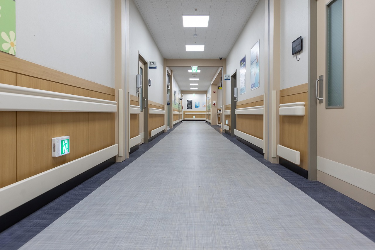 Un long couloir d’hôpital vide et éclairé, aux murs clairs bordés de rampes en bois